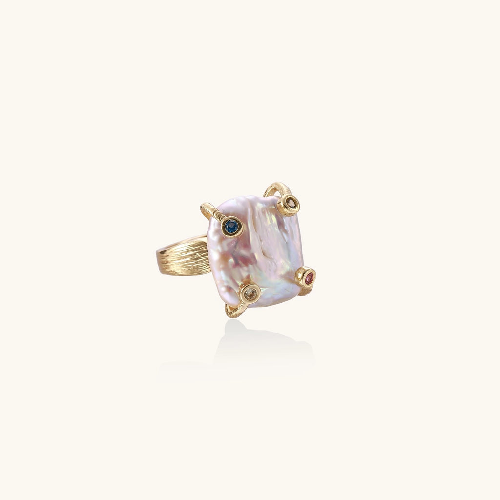Gold-plated ring featuring large baroque freshwater pearl with small colorful gemstone accents on textured band
