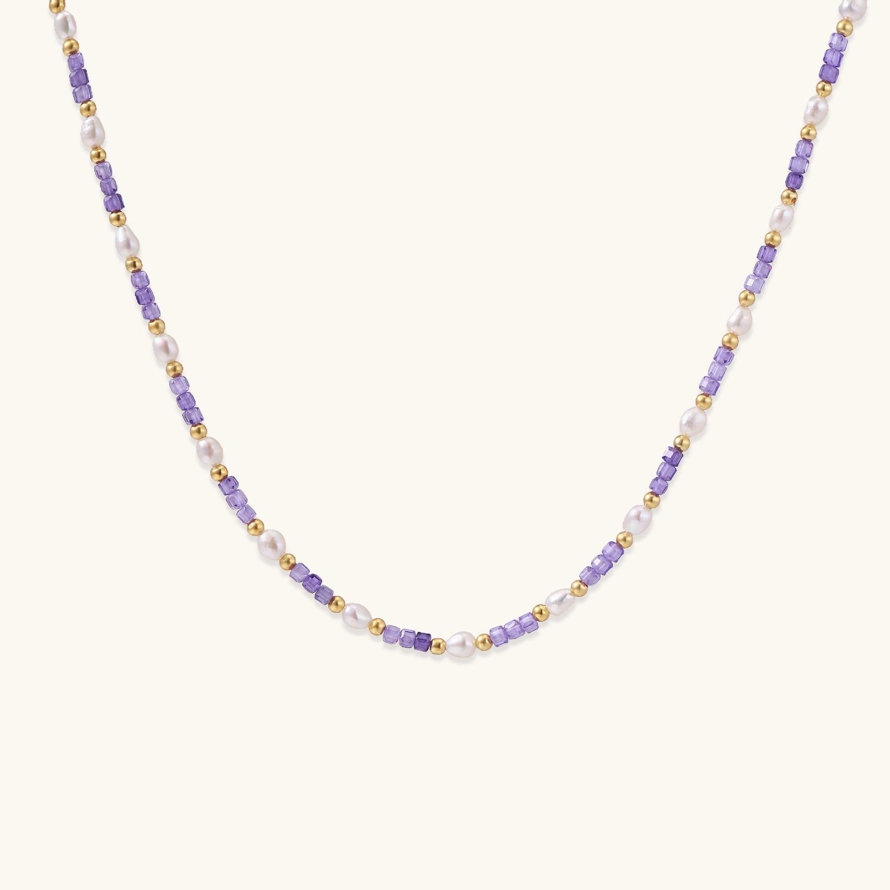 Delicate beaded necklace with alternating purple zirconia stones, white freshwater pearls, and gold-plated spacers on cream background.