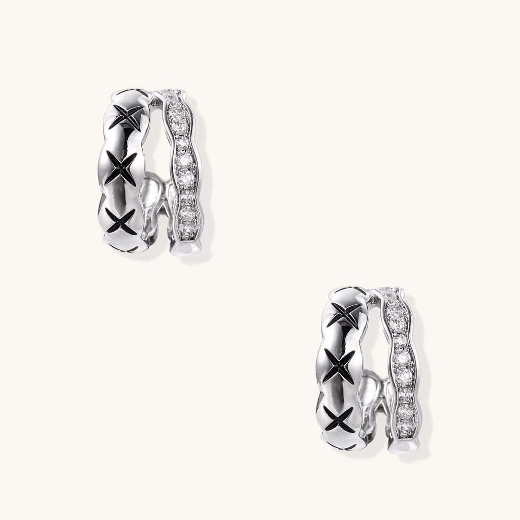 Close-up of gold-plated huggie earrings featuring X-pattern band and wavy zirconia-set band on white background.