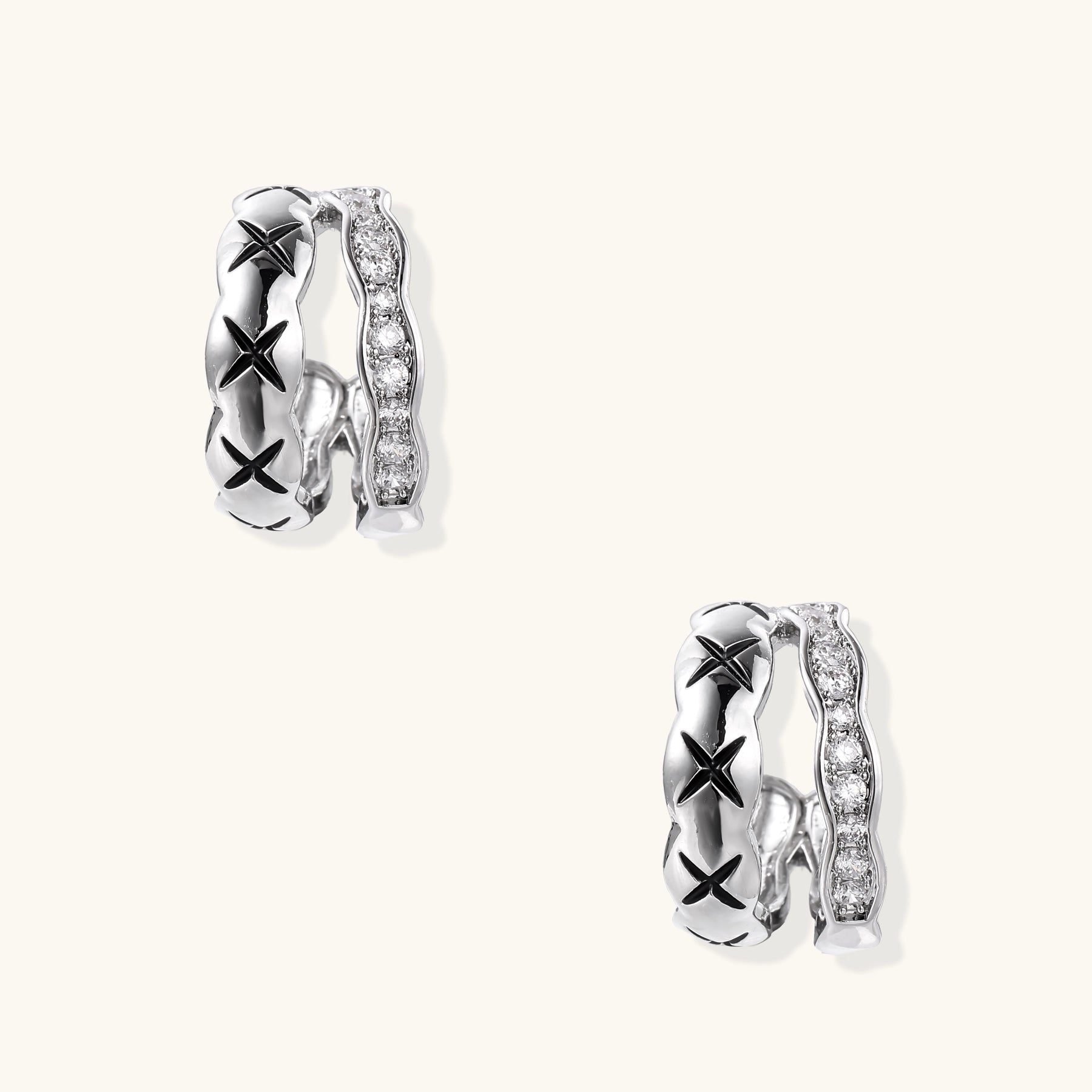 Close-up of gold-plated huggie earrings featuring X-pattern band and wavy zirconia-set band on white background.