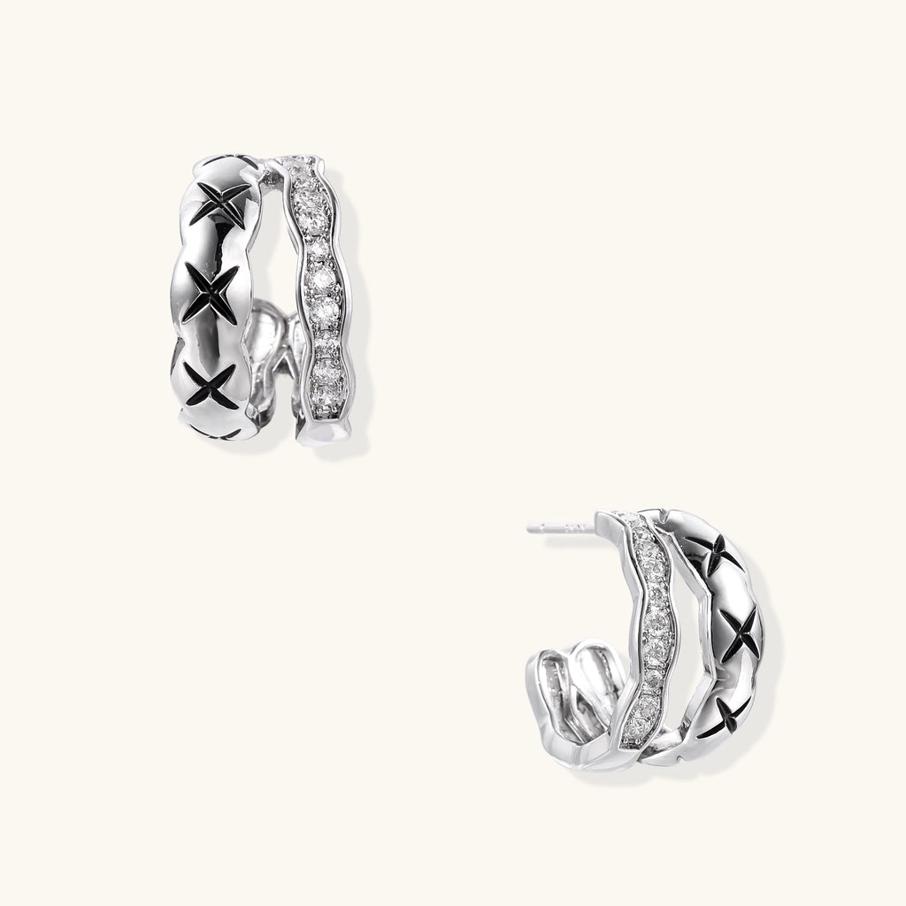 Close-up of gold-plated huggie earrings featuring X-pattern band and wavy zirconia-set band on white background.