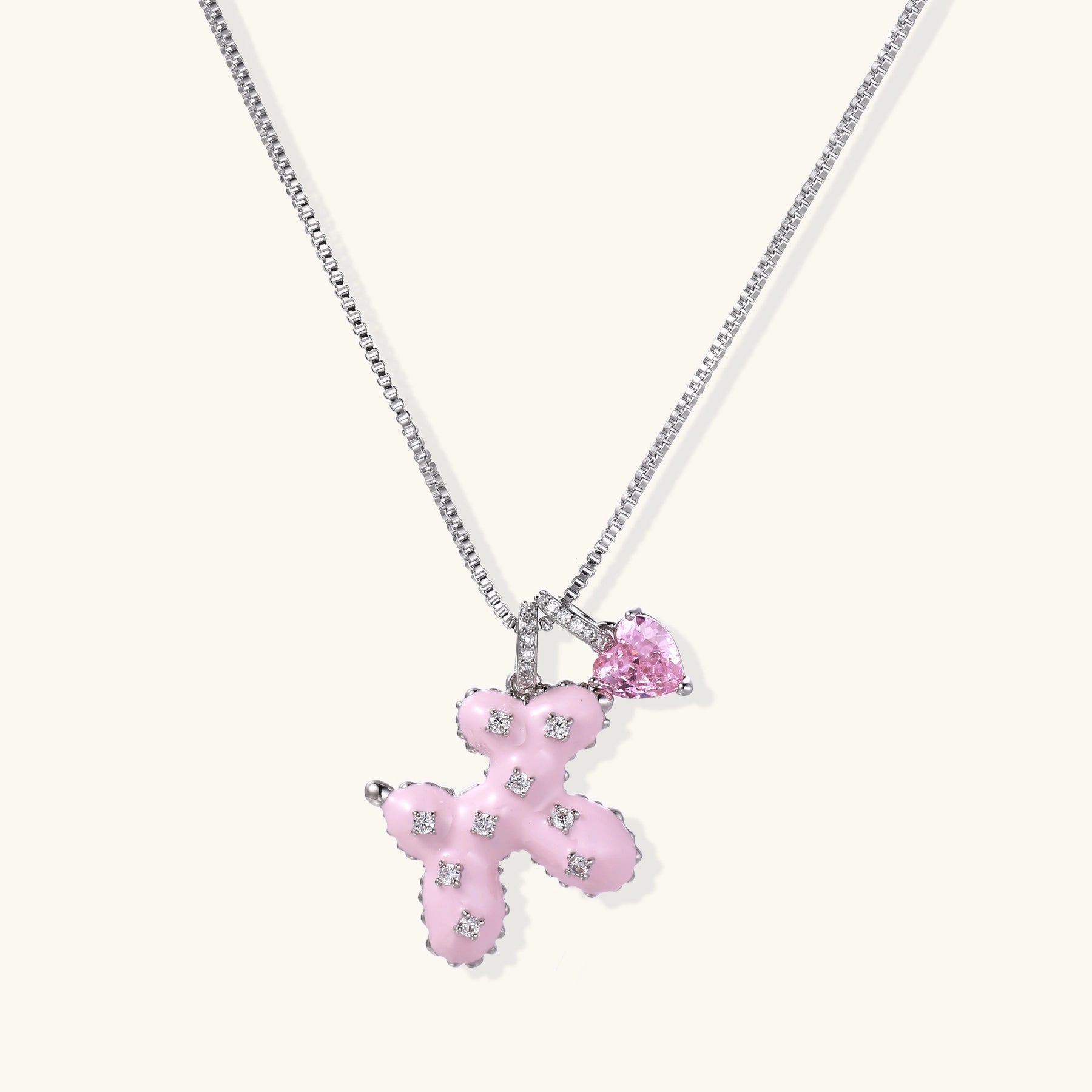 Pink enamel cross pendant with zirconia crystals and teardrop charm on 18K gold-plated chain against white background