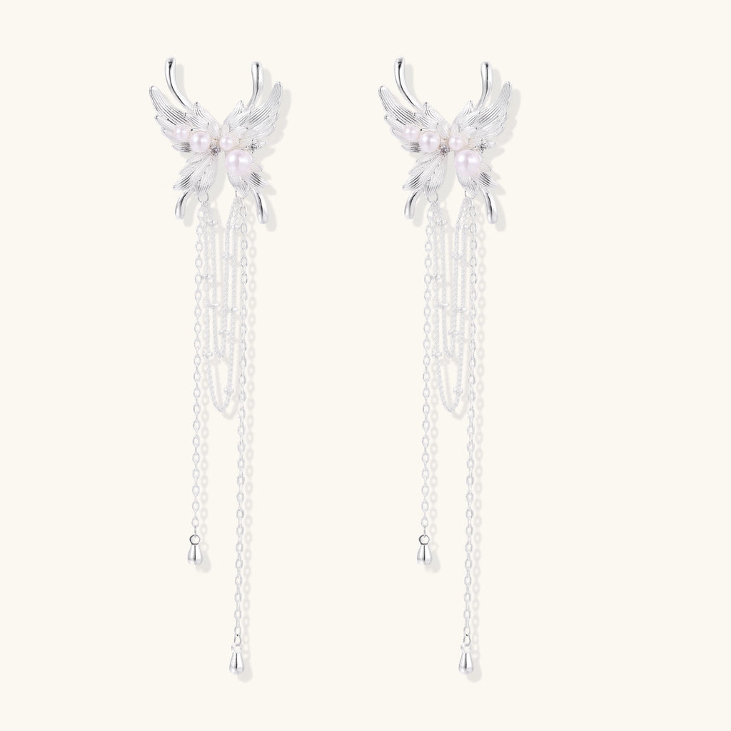 Elegant silver-plated drop earrings with wing-shaped tops, white pearl accents, and long chain tassels on white background.