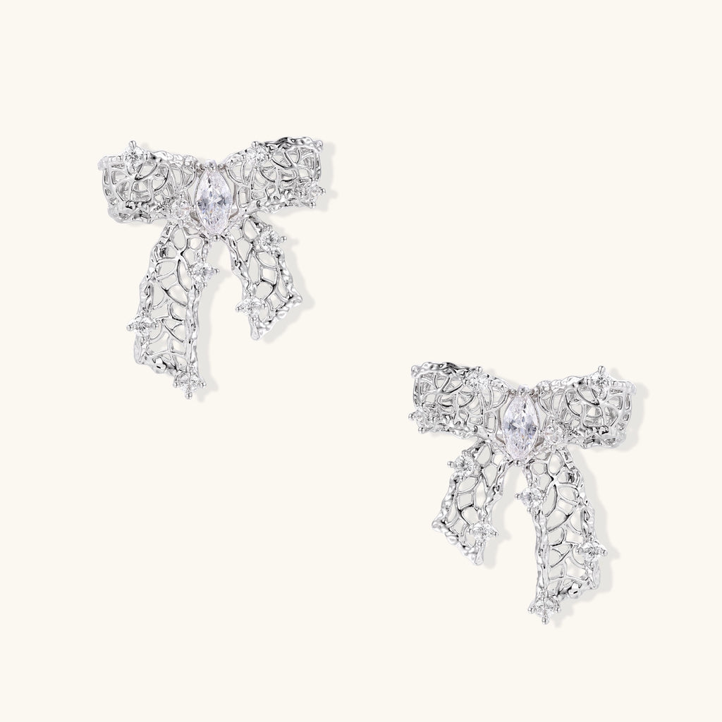 Gold and silver bow-shaped earrings with intricate lattice pattern and clear zirconia stones on neutral background.