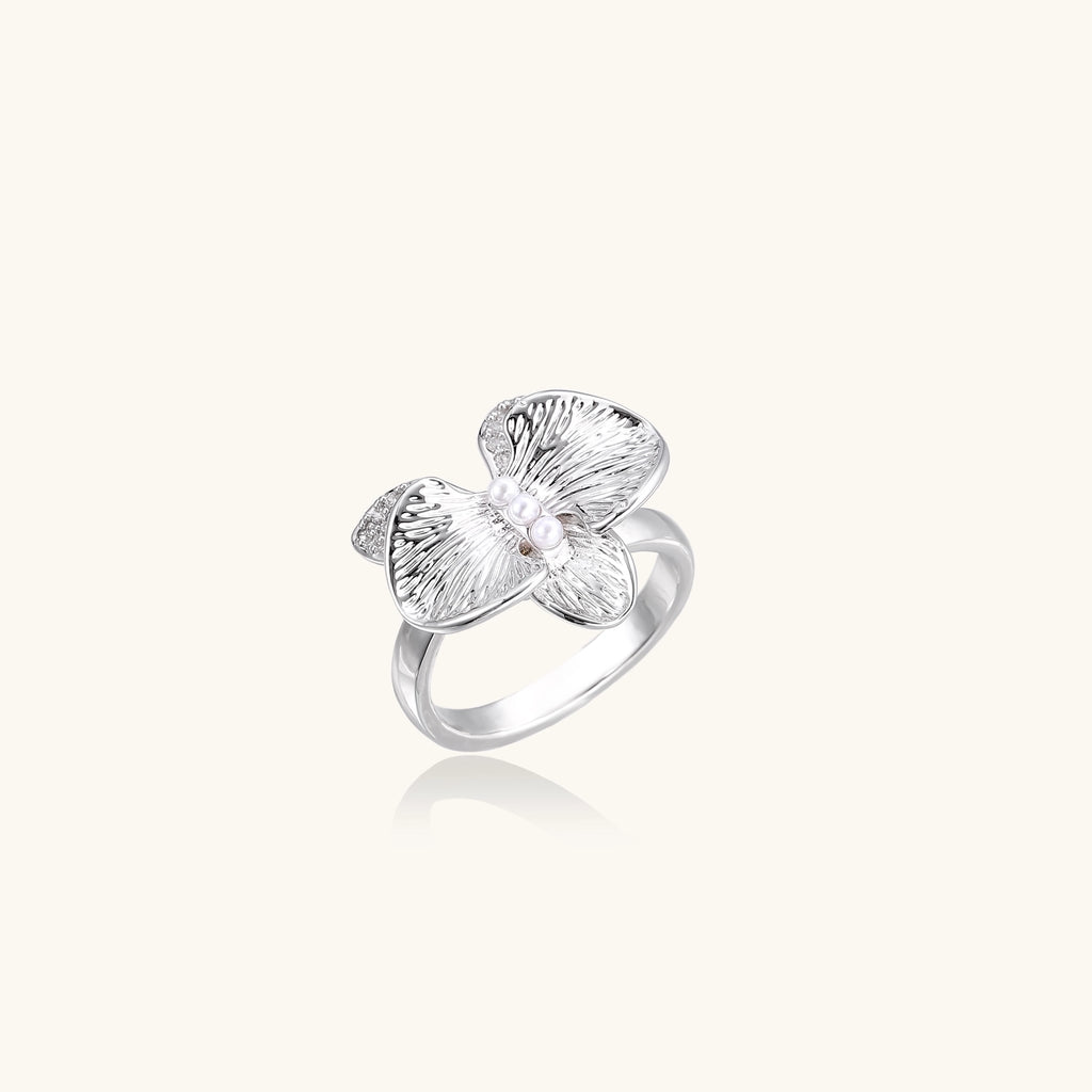 Gold-plated brass ring with textured orchid petals, zirconia stones, and center pearls on white background.