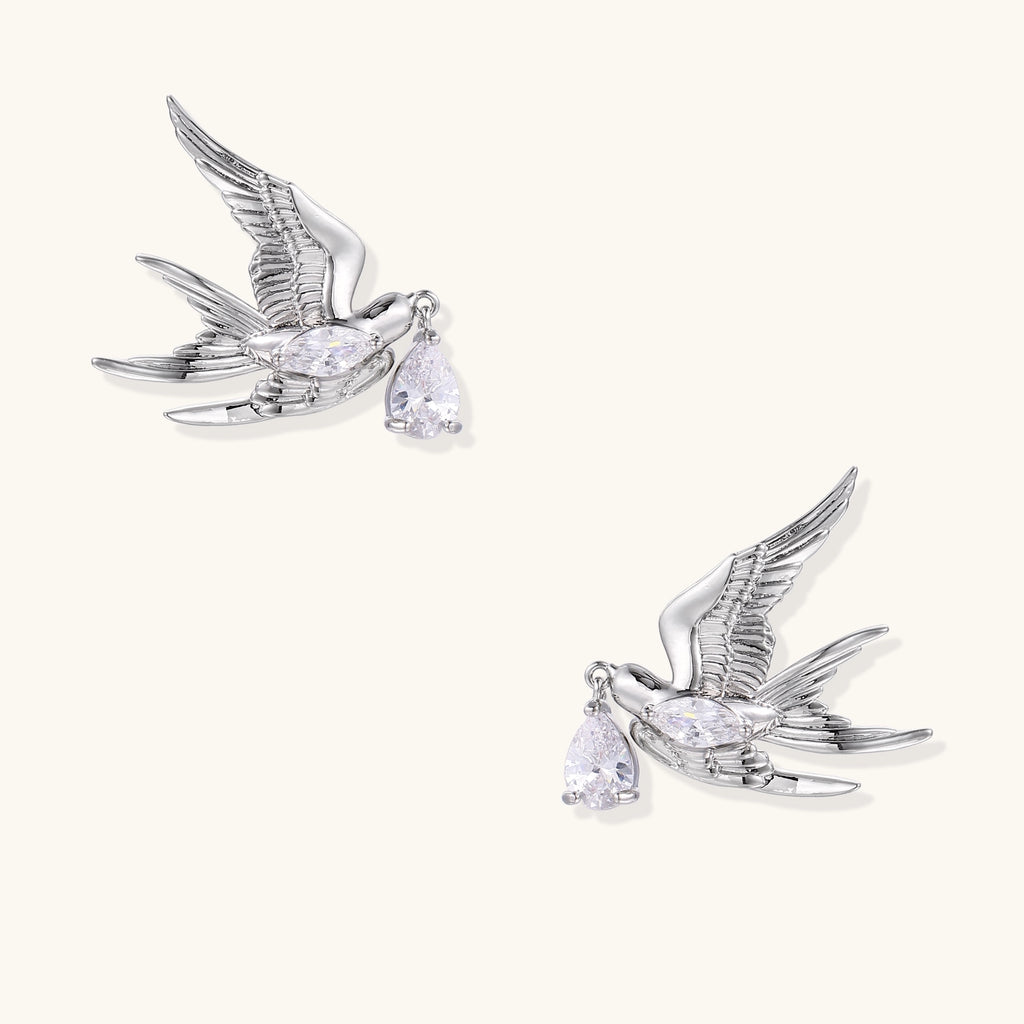 Gold-plated brass swallow earrings with detailed wing engravings carrying clear zirconia crystal drops in their beaks