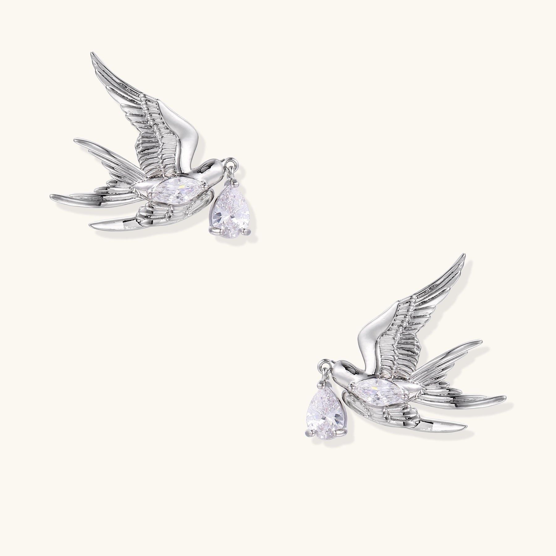 Gold-plated brass swallow earrings with detailed wing engravings carrying clear zirconia crystal drops in their beaks