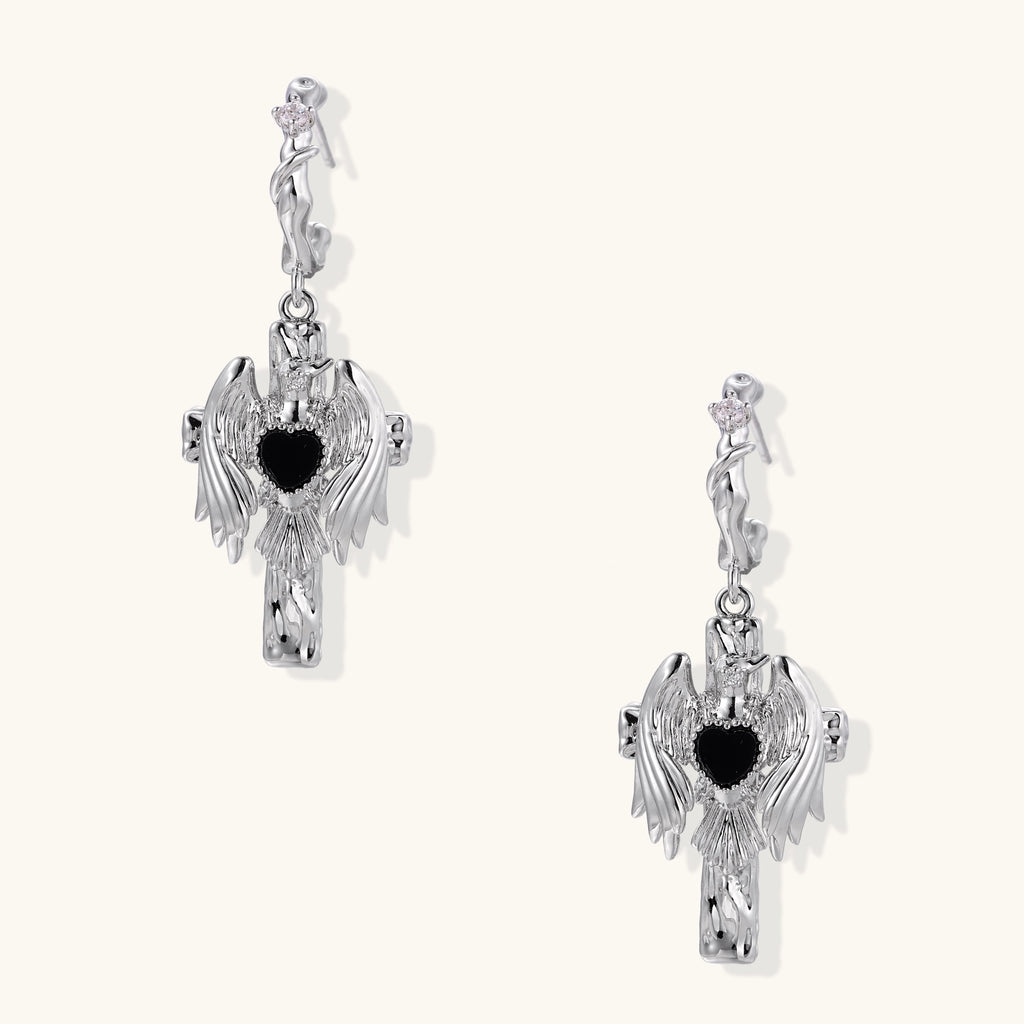 Gold-plated brass earrings with winged design, black heart-shaped zirconia center, and crystal accents on white background.