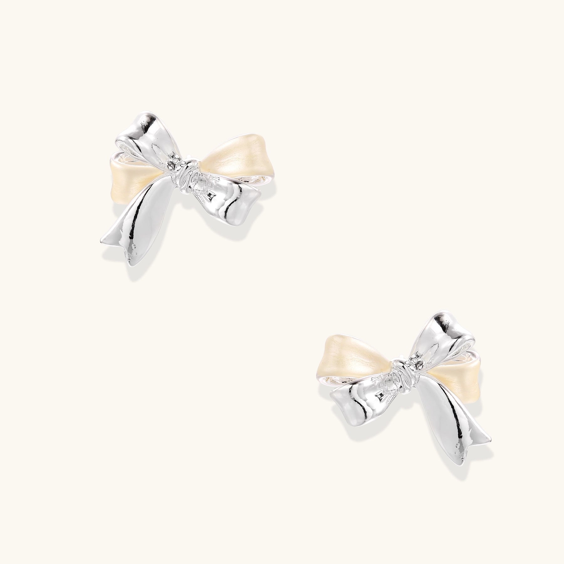 Close-up of bow-shaped stud earrings with 18K gold plated brass and silver details on white background.