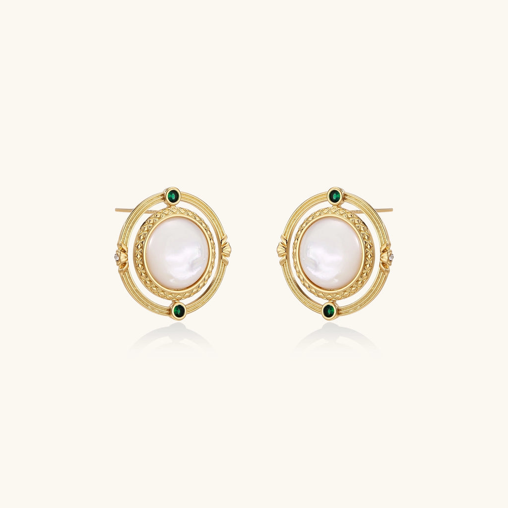 Close-up of gold-plated circular earrings with white mother-of-pearl centers and green zirconia accents on cream background.