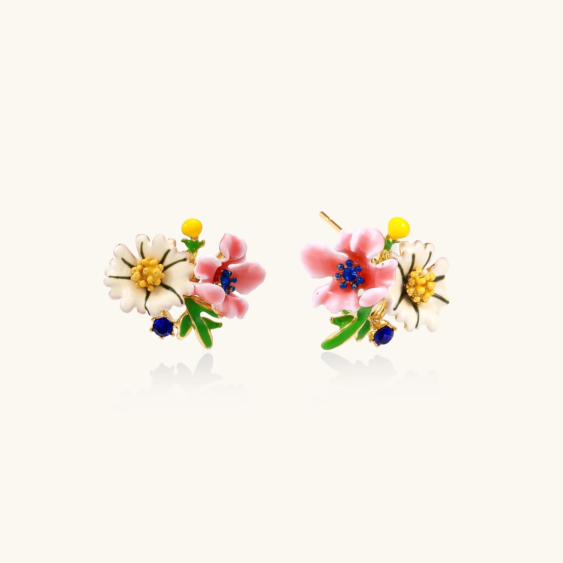 Detailed view of gold-plated brass stud earrings featuring multicolor enamel flowers with white, pink, and blue petals