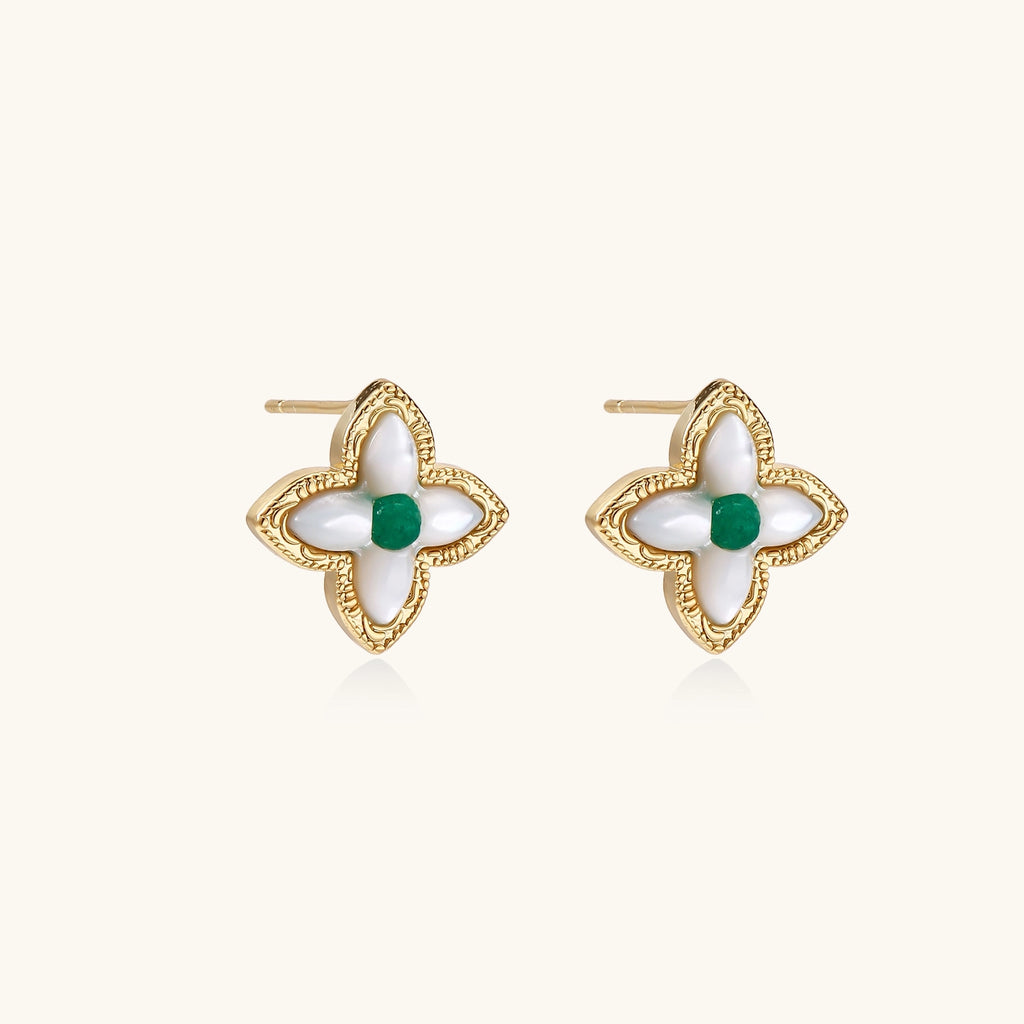 Dainty gold-plated quatrefoil stud earrings with white mother-of-pearl petals and green gemstone centers on beige background.