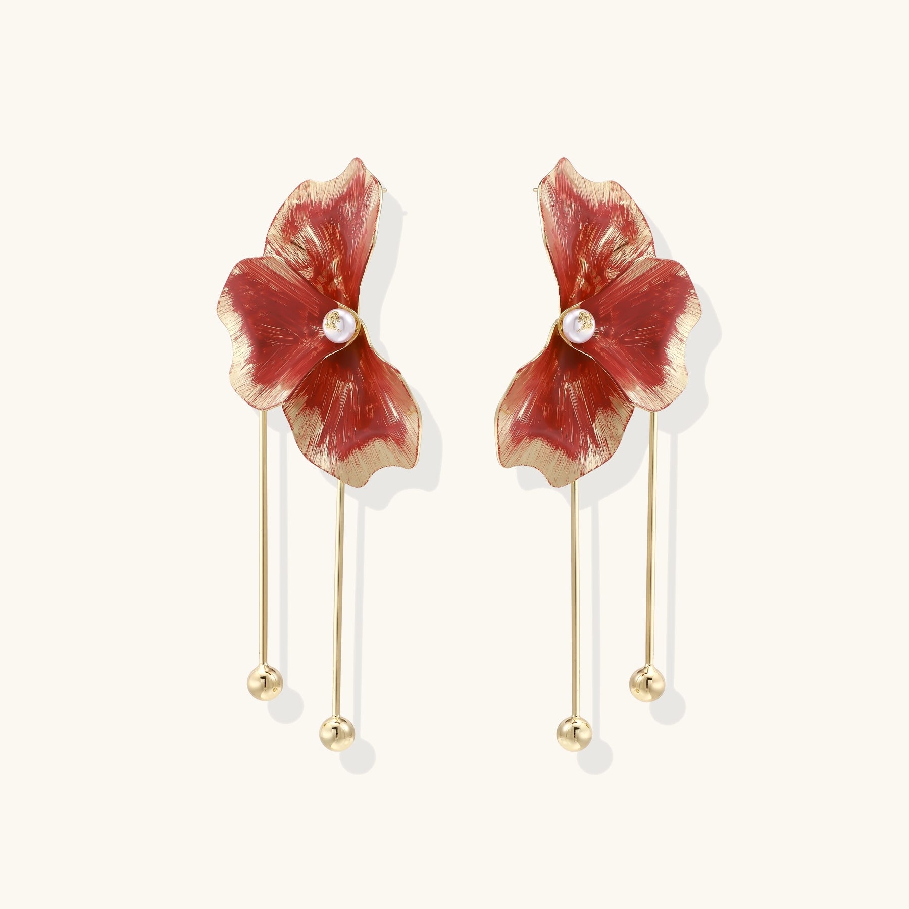 Statement drop earrings with coral-red enamel flower petals, gold-plated brass, and mother-of-pearl centers on white background