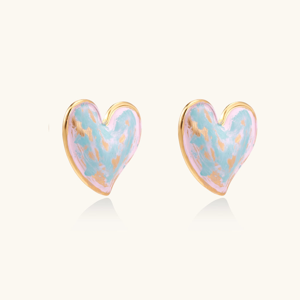 Heart-shaped stud earrings with iridescent blue-pink enamel finish and gold-plated brass frames against cream background