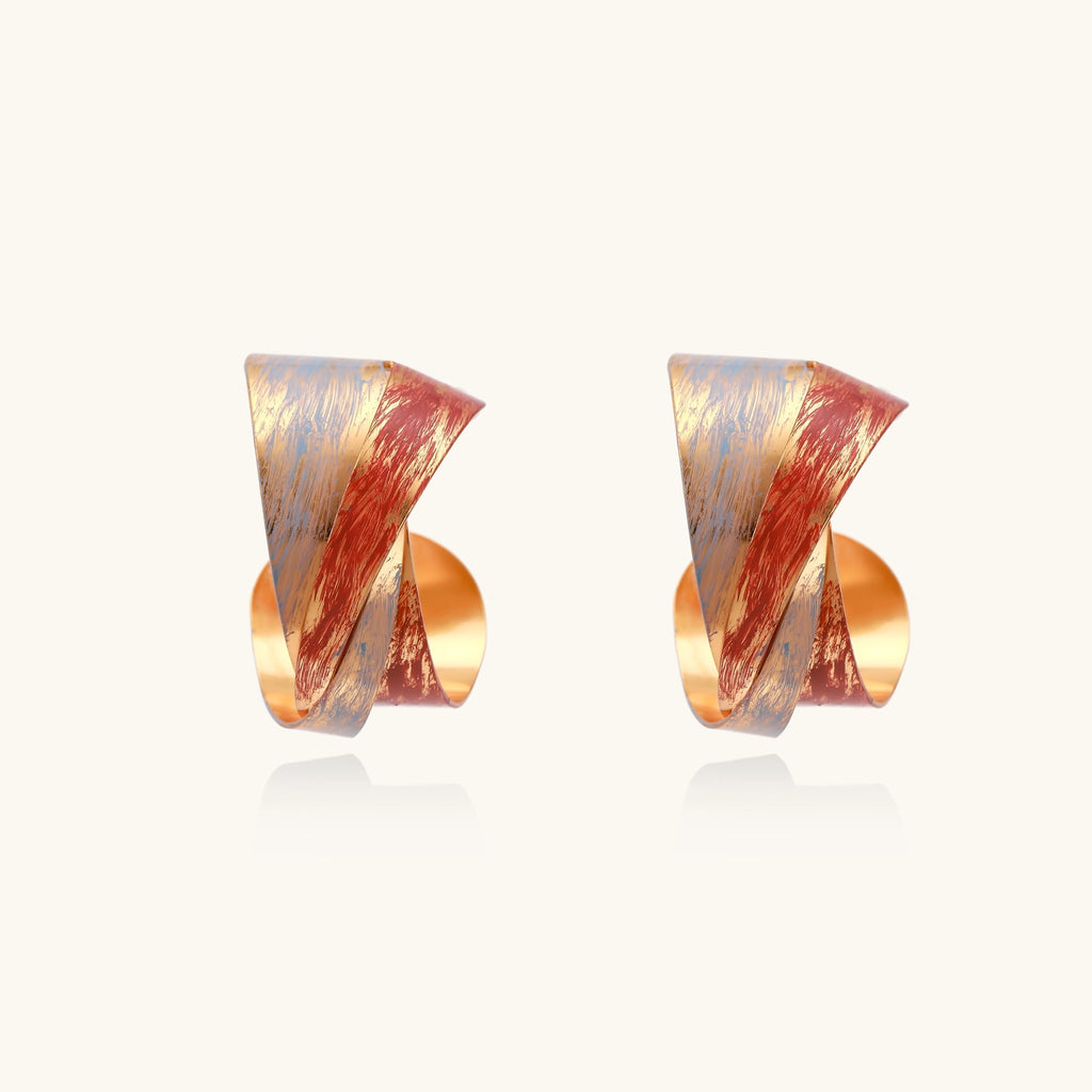 Twisted gold-plated brass earrings with multicolored enamel brushstroke patterns in burgundy and blue on white background.