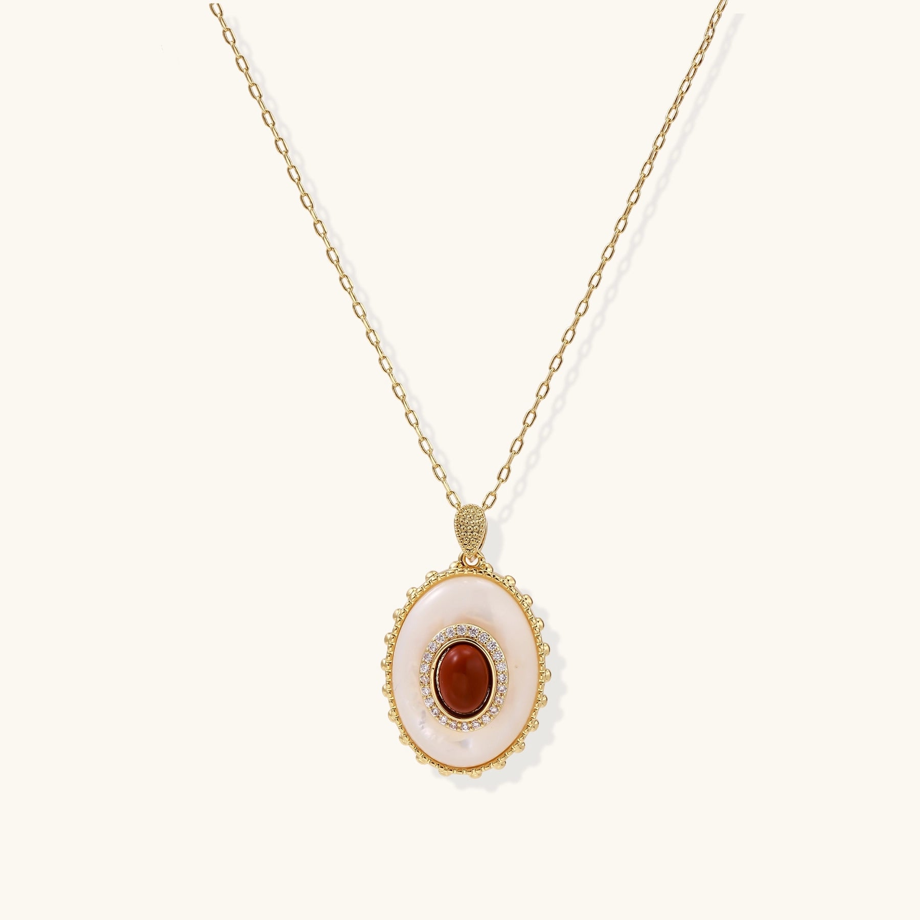 Oval gold-plated pendant featuring mother-of-pearl base with carnelian center stone and crystal accents on delicate chain