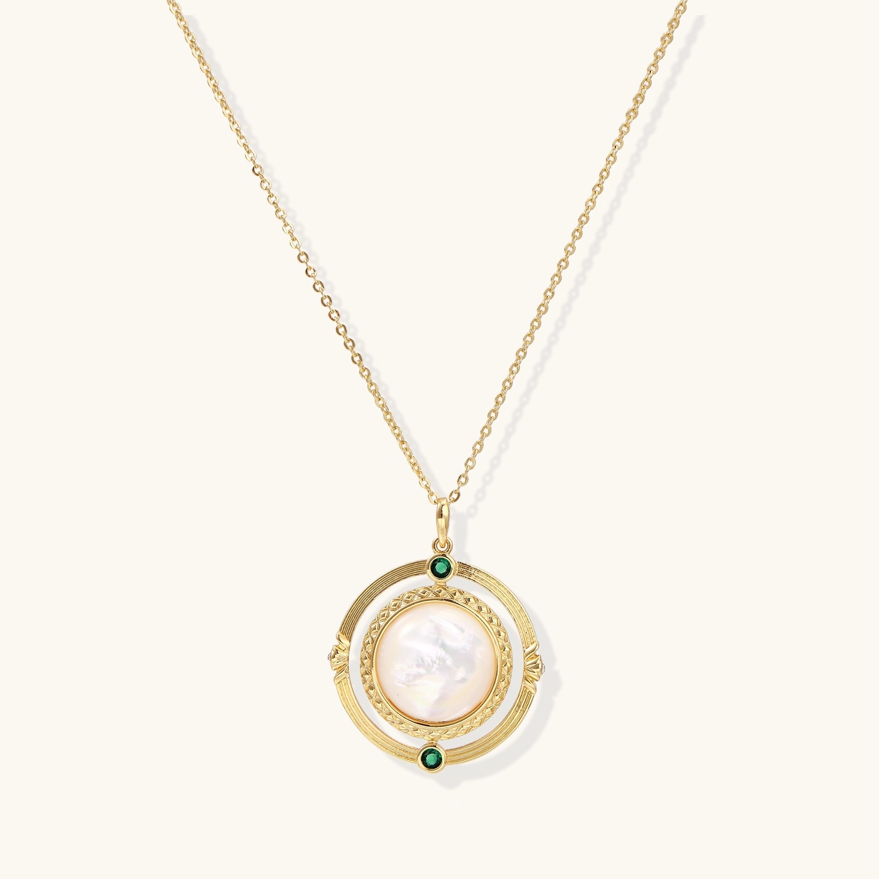 Gold-plated pendant necklace with circular orbital design, iridescent mother-of-pearl center and green zirconia accents