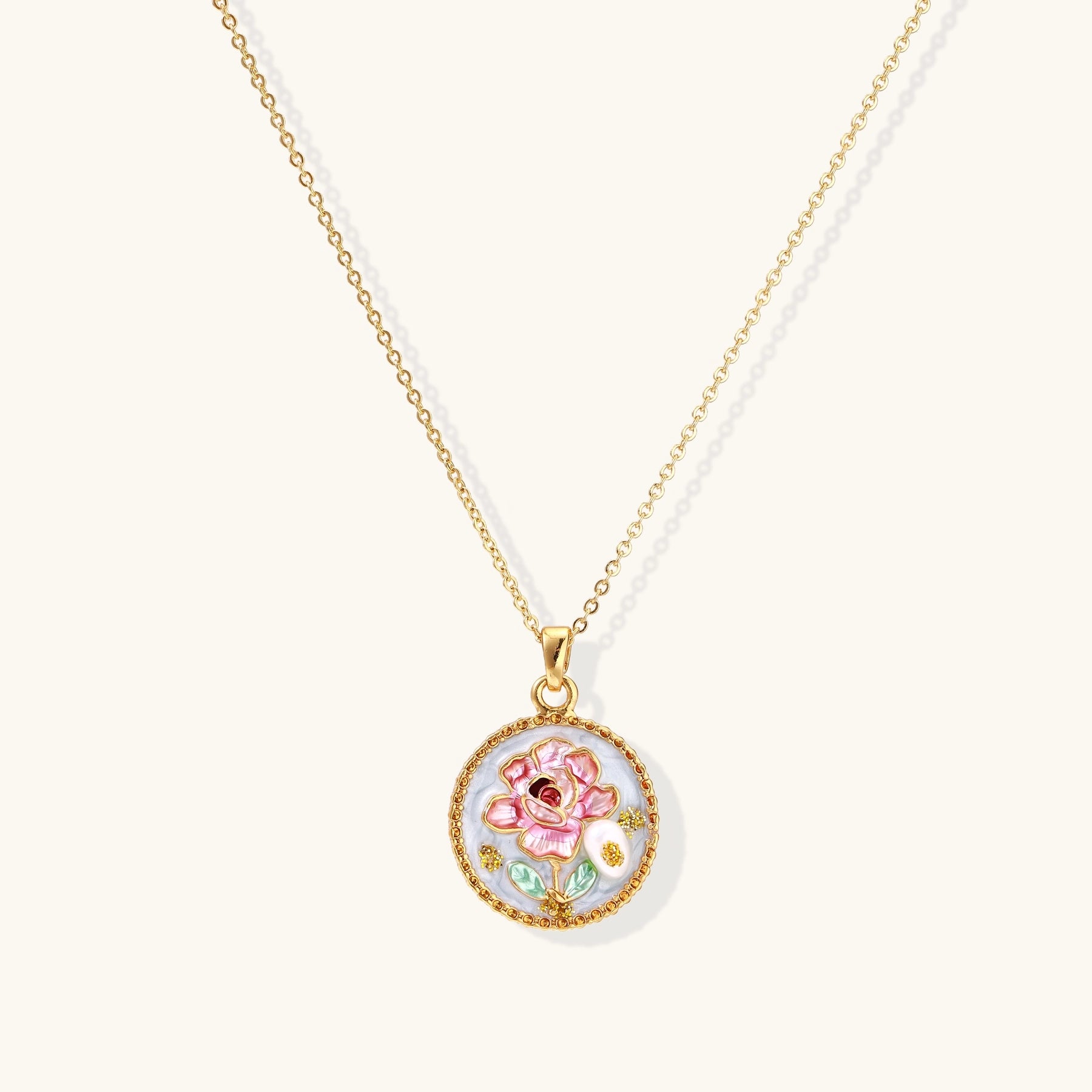 Gold-plated circular pendant featuring pink enamel rose with pearl accents and green leaf details on adjustable chain.