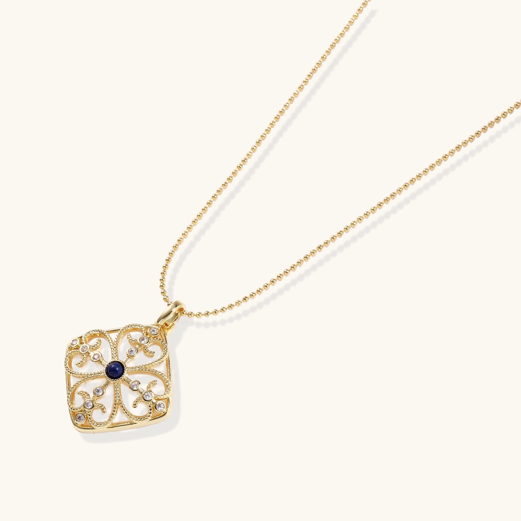 Gold-plated square pendant with ornate scrollwork featuring central blue lapis lazuli stone on ball chain