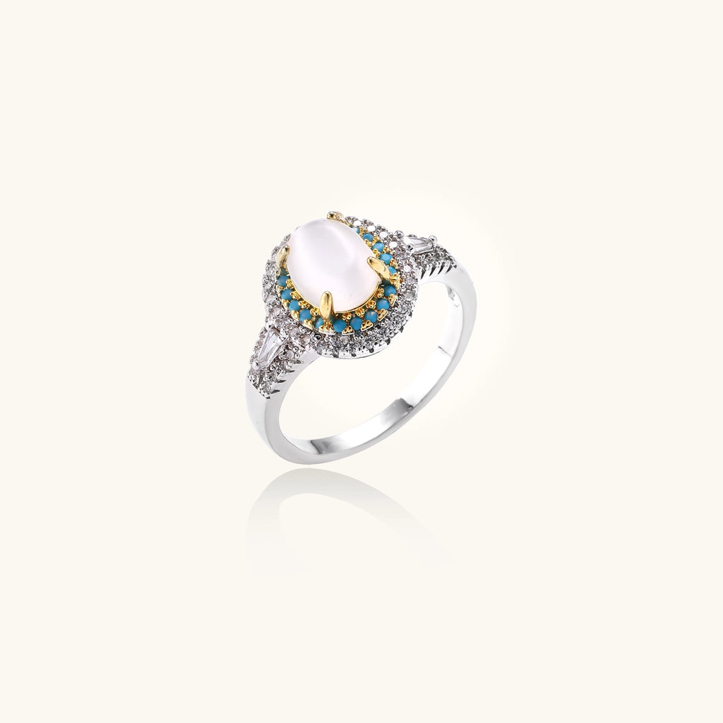 Gold-plated ring with oval cat's eye stone center, blue accent stones, and crystal halo on white background.