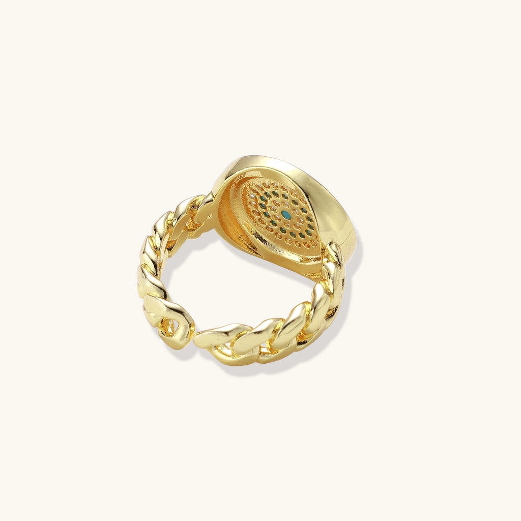 Gold-plated brass ring with Greek key border, evil eye center, and turquoise cubic zirconia stones in chunky chain band style.