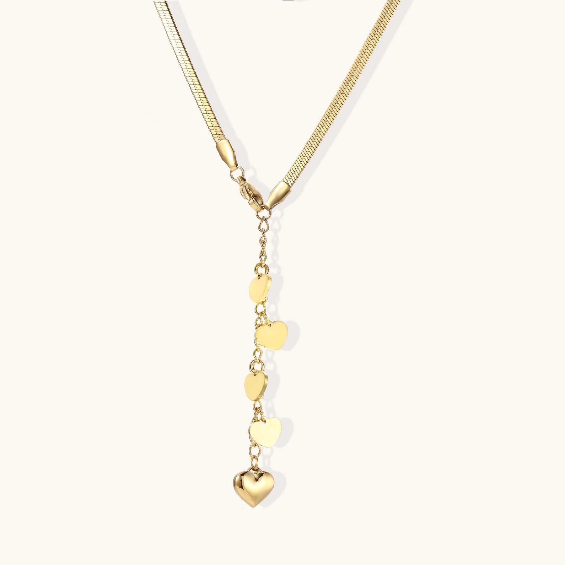 Gold-plated necklace with cascading heart charms in graduated sizes on herringbone chain against white background.