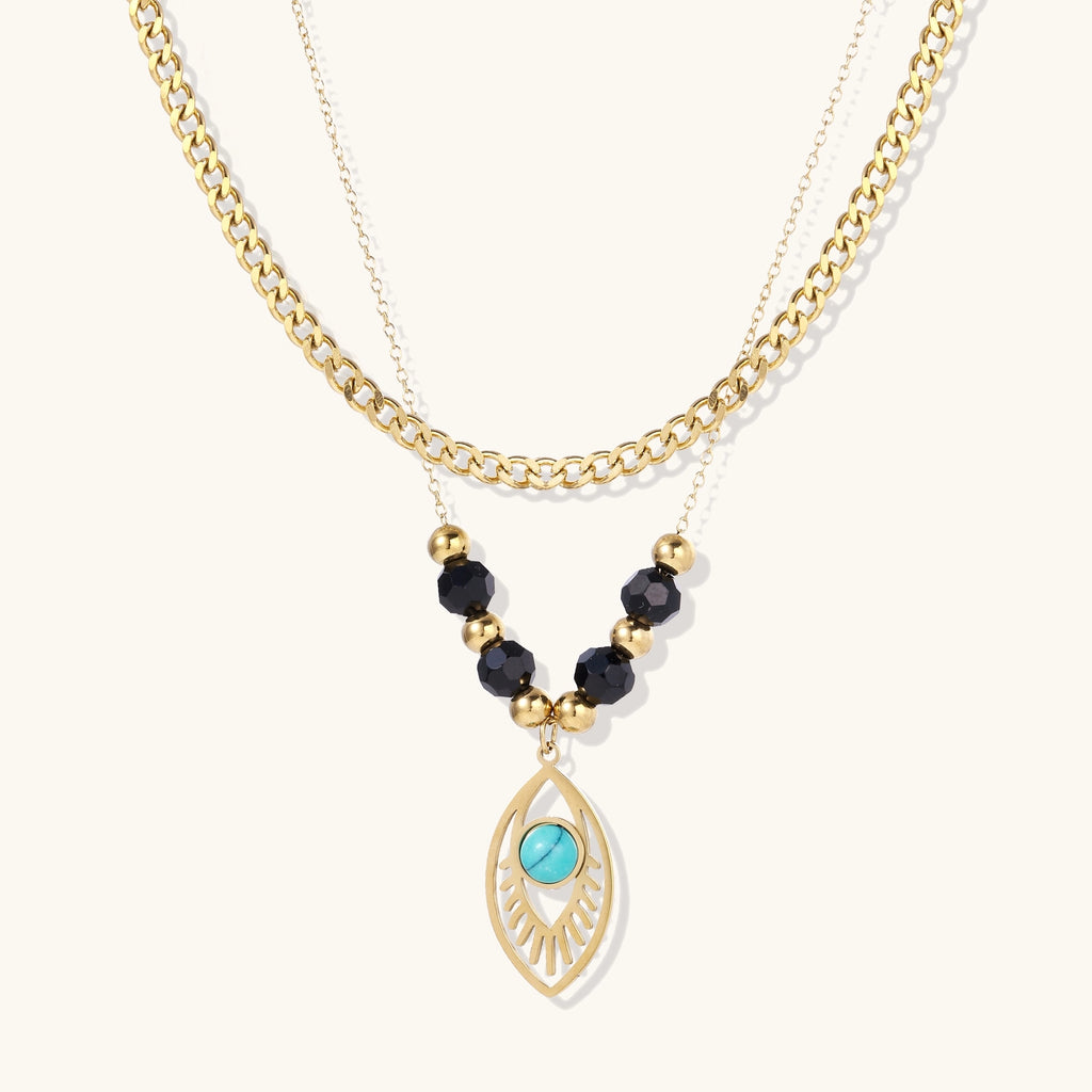 Gold layered necklace set with evil eye pendant, turquoise center stone, and black beaded chain on cream background