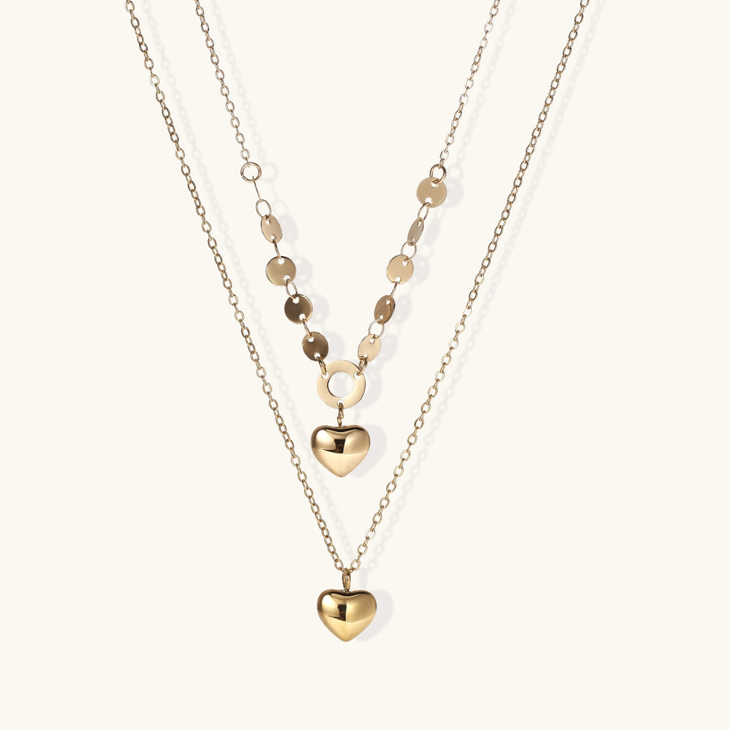 Three-layer gold-plated necklace set with disc chain and two heart pendants on neutral background