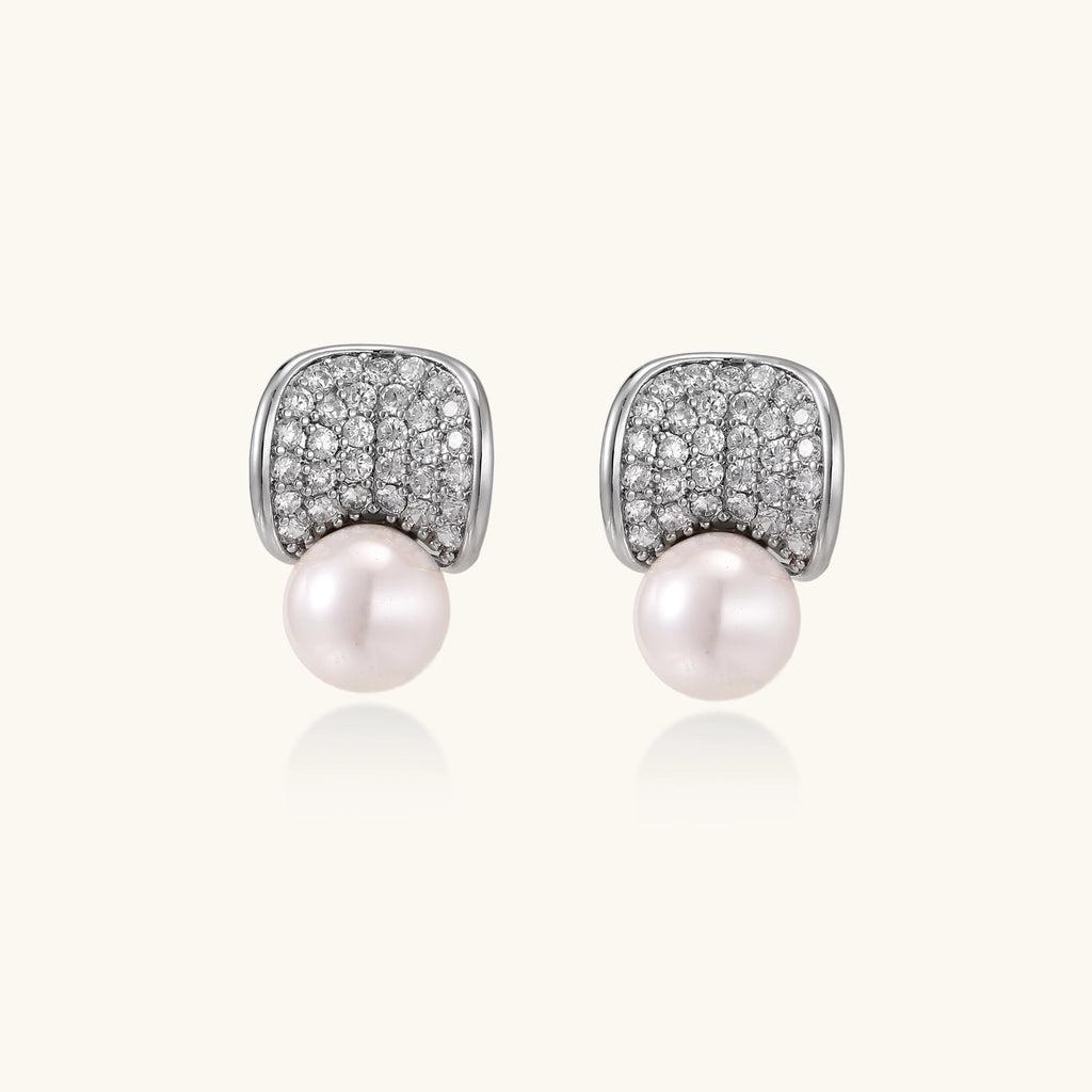 Elegant gold-plated curved earrings with diamond pavé crescents and suspended freshwater pearls on neutral background.