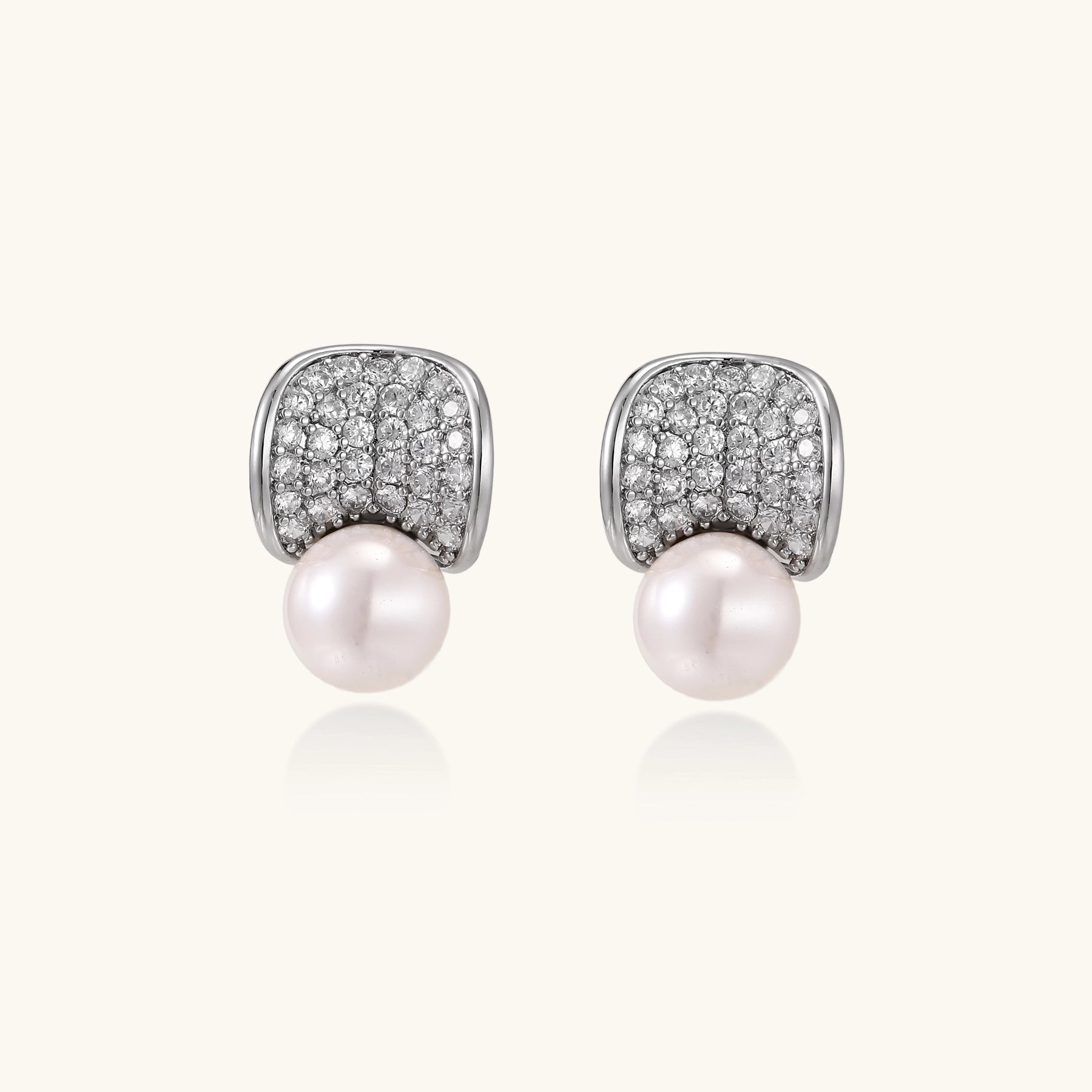 Elegant gold-plated curved earrings with diamond pavé crescents and suspended freshwater pearls on neutral background.