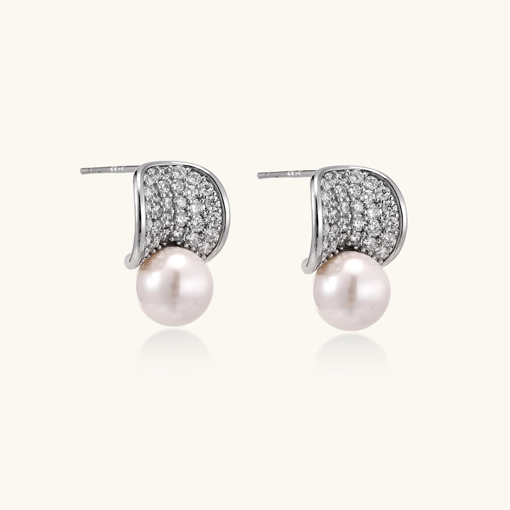 Elegant gold-plated curved earrings with diamond pavé crescents and suspended freshwater pearls on neutral background.