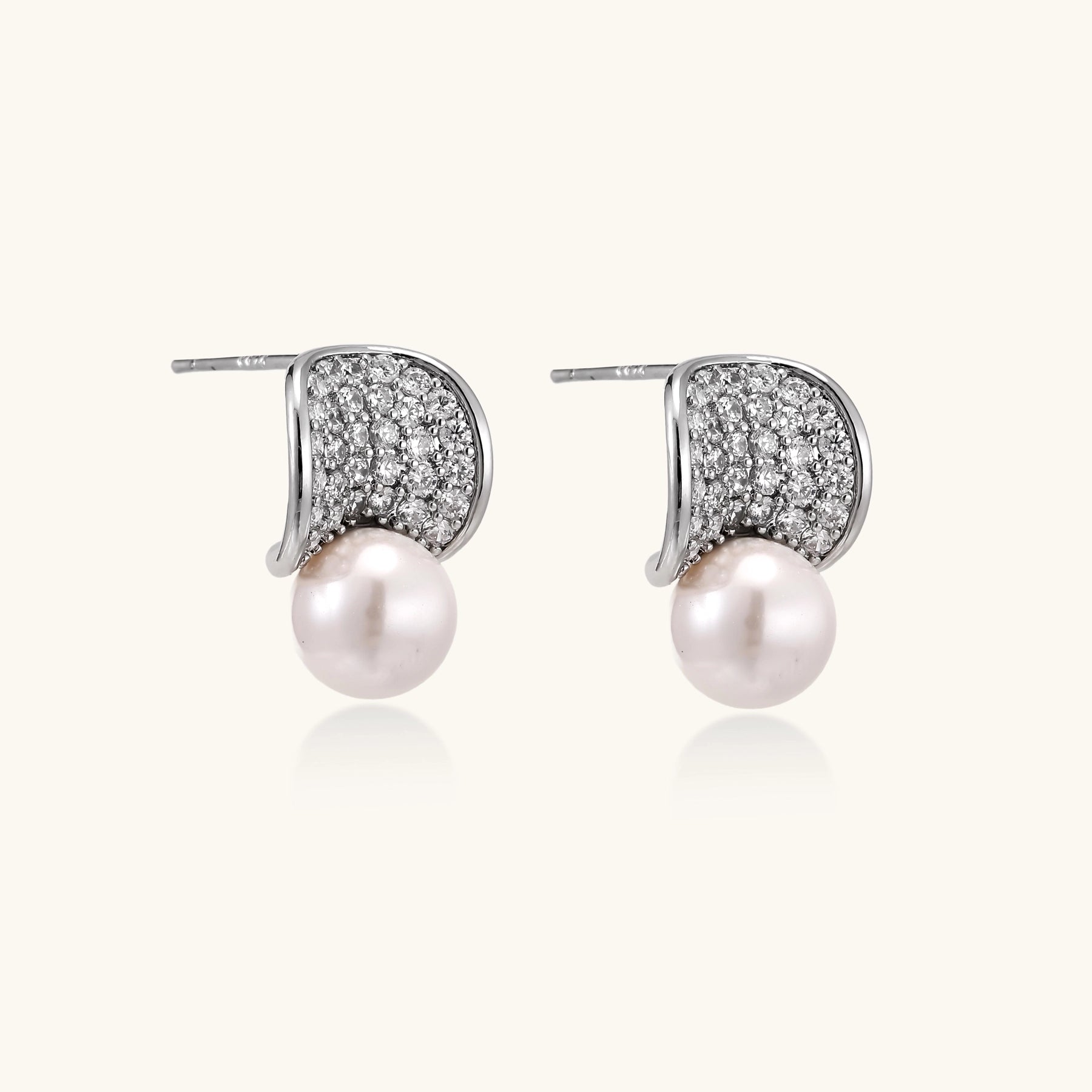 Elegant gold-plated curved earrings with diamond pavé crescents and suspended freshwater pearls on neutral background.