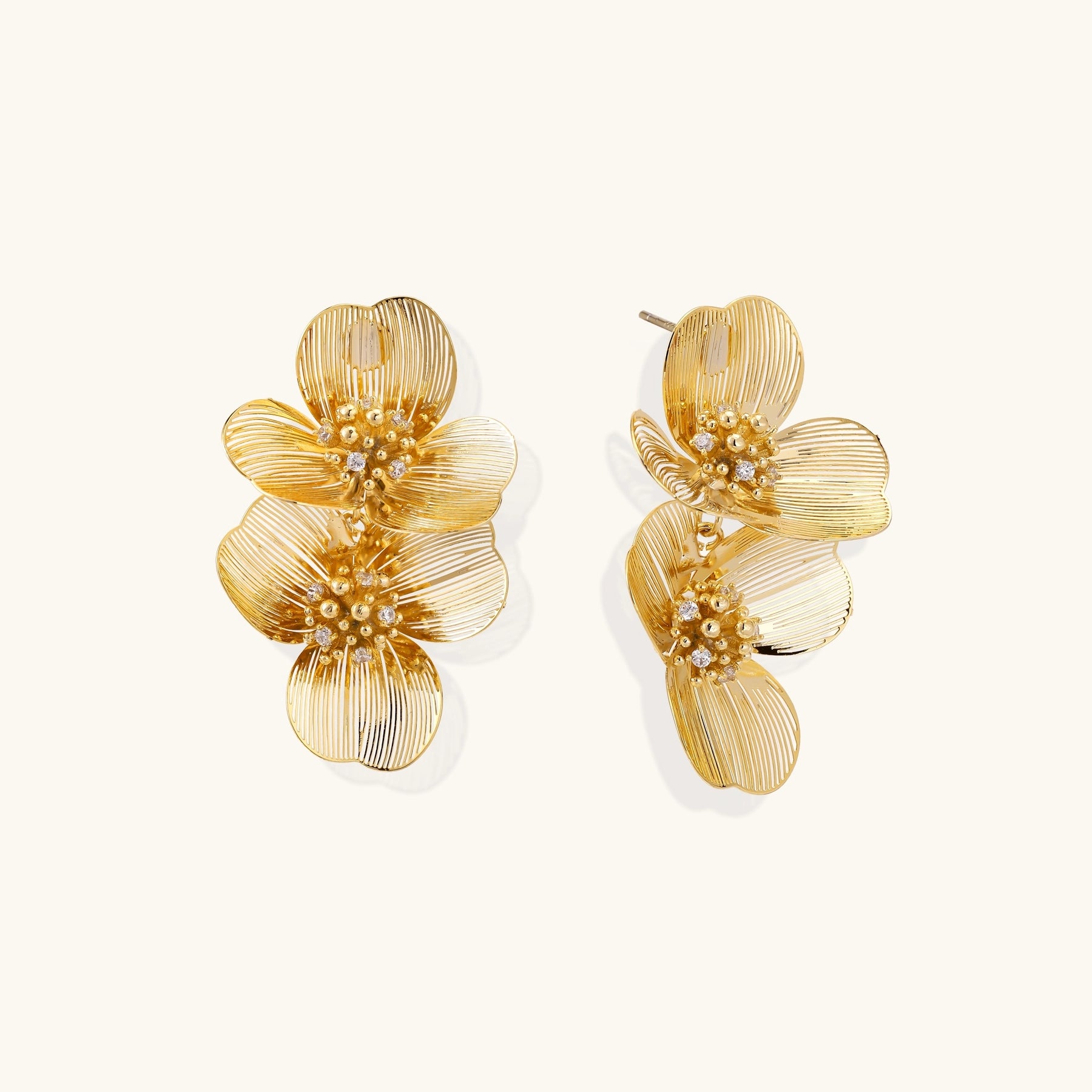 Layered gold-plated floral stud earrings with textured petals and crystal-accented centers on white background.