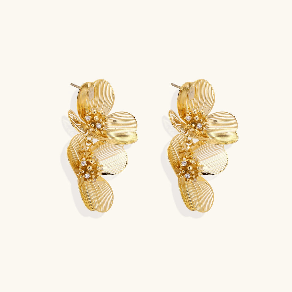 Layered gold-plated floral stud earrings with textured petals and crystal-accented centers on white background.