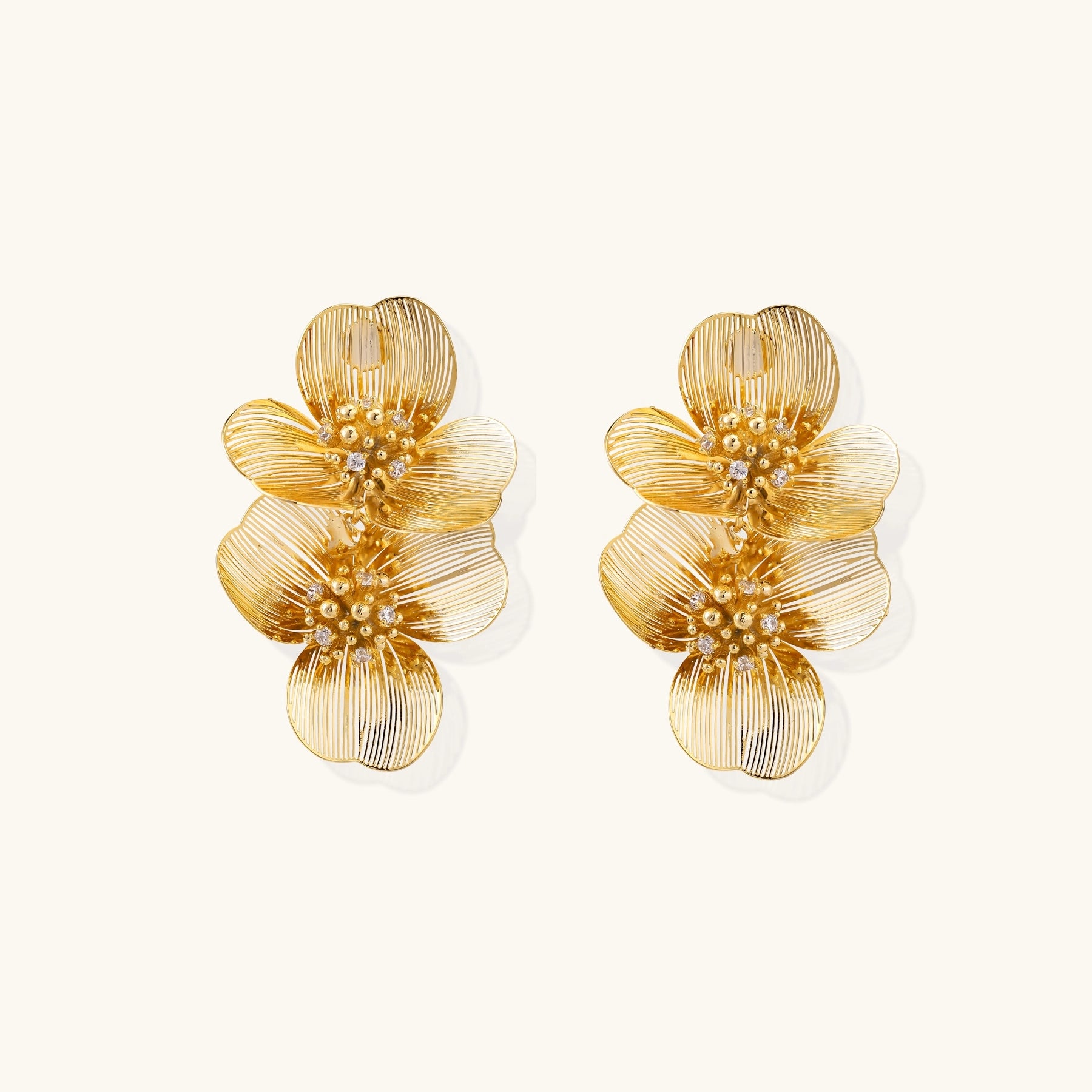 Layered gold-plated floral stud earrings with textured petals and crystal-accented centers on white background.