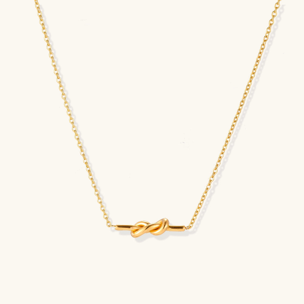 Dainty 18K gold plated stainless steel chain necklace with minimalist knot pendant on cream background.