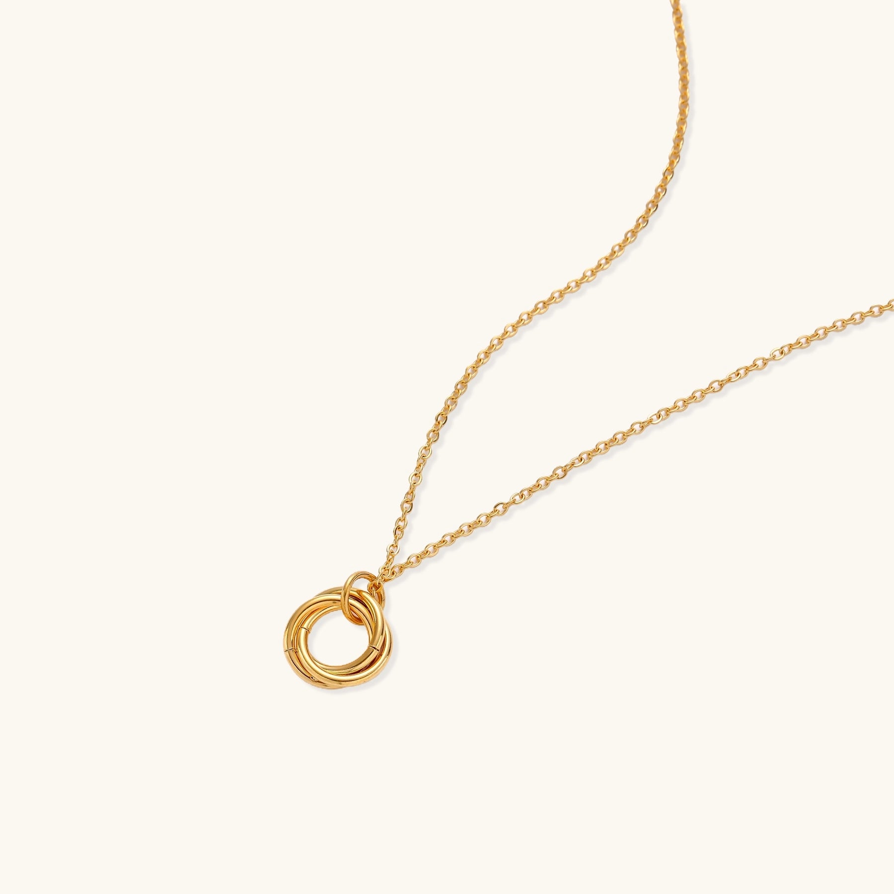 Close-up of a gold-plated stainless steel necklace with interlocking twisted ring pendant on white background