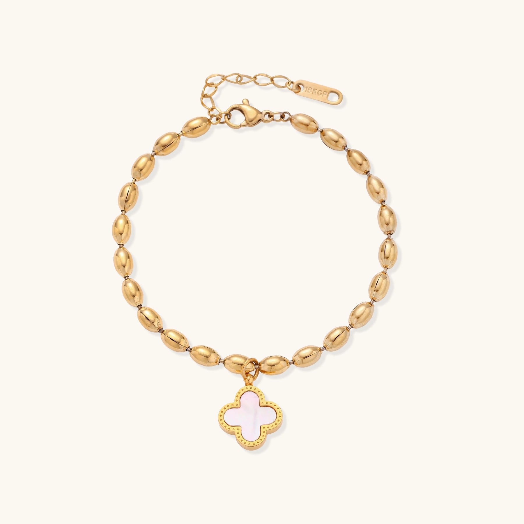 Dainty gold-plated beaded bracelet with oval links and four-leaf clover charm pendant on neutral background.