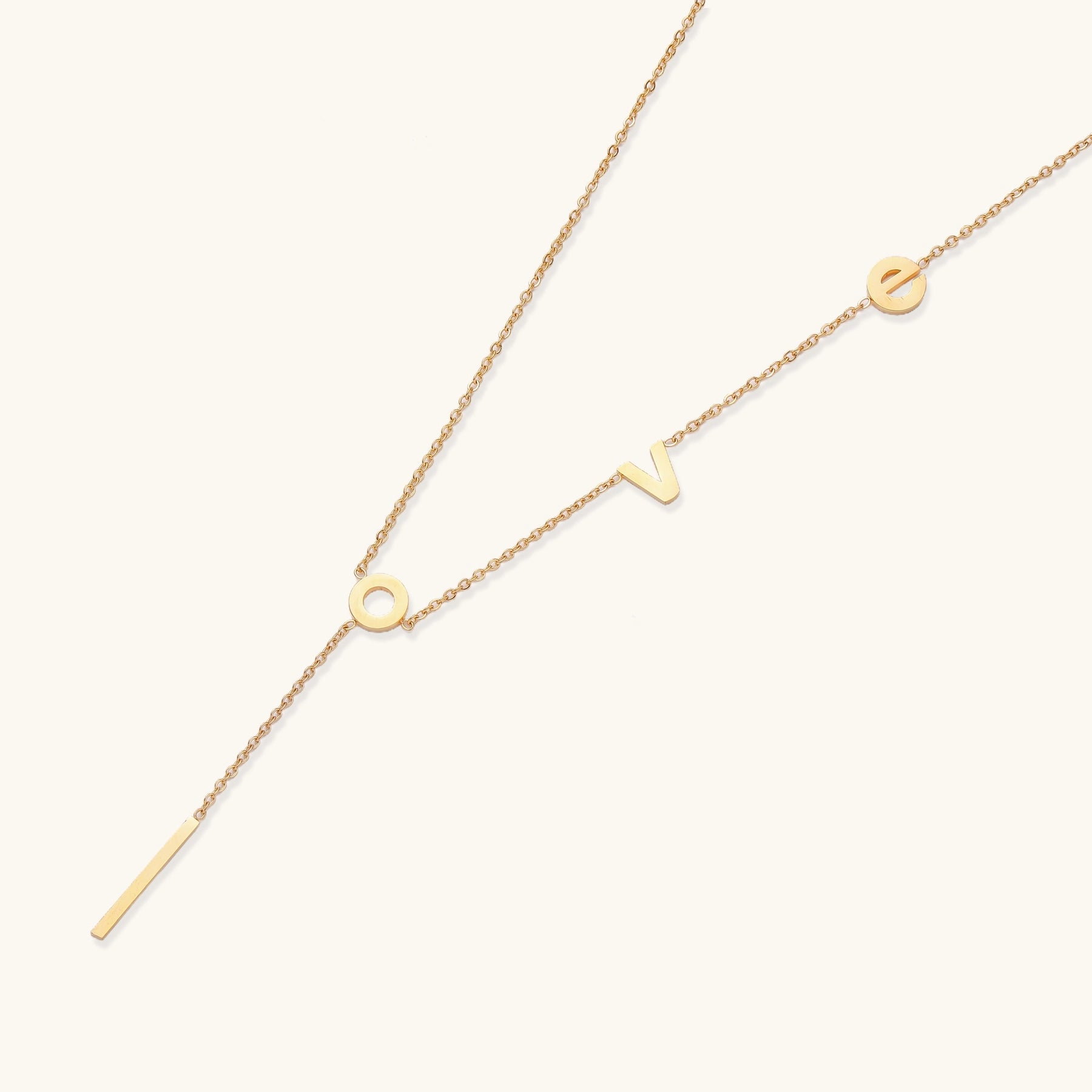 Gold-plated lariat necklace spelling LOVE with letter charms and vertical bar pendant on white background.