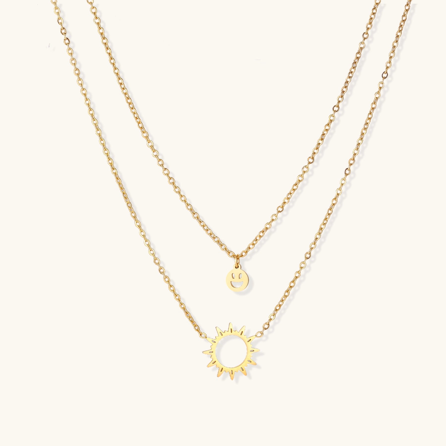 Delicate gold-plated layered necklace with smiley face and sun pendants on white background, showing adjustable chain.