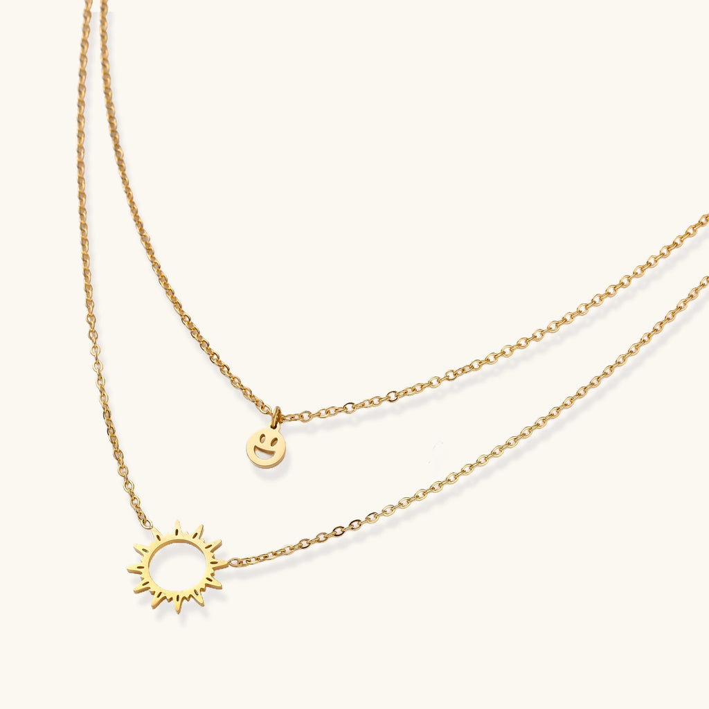 Delicate gold-plated layered necklace with smiley face and sun pendants on white background, showing adjustable chain.