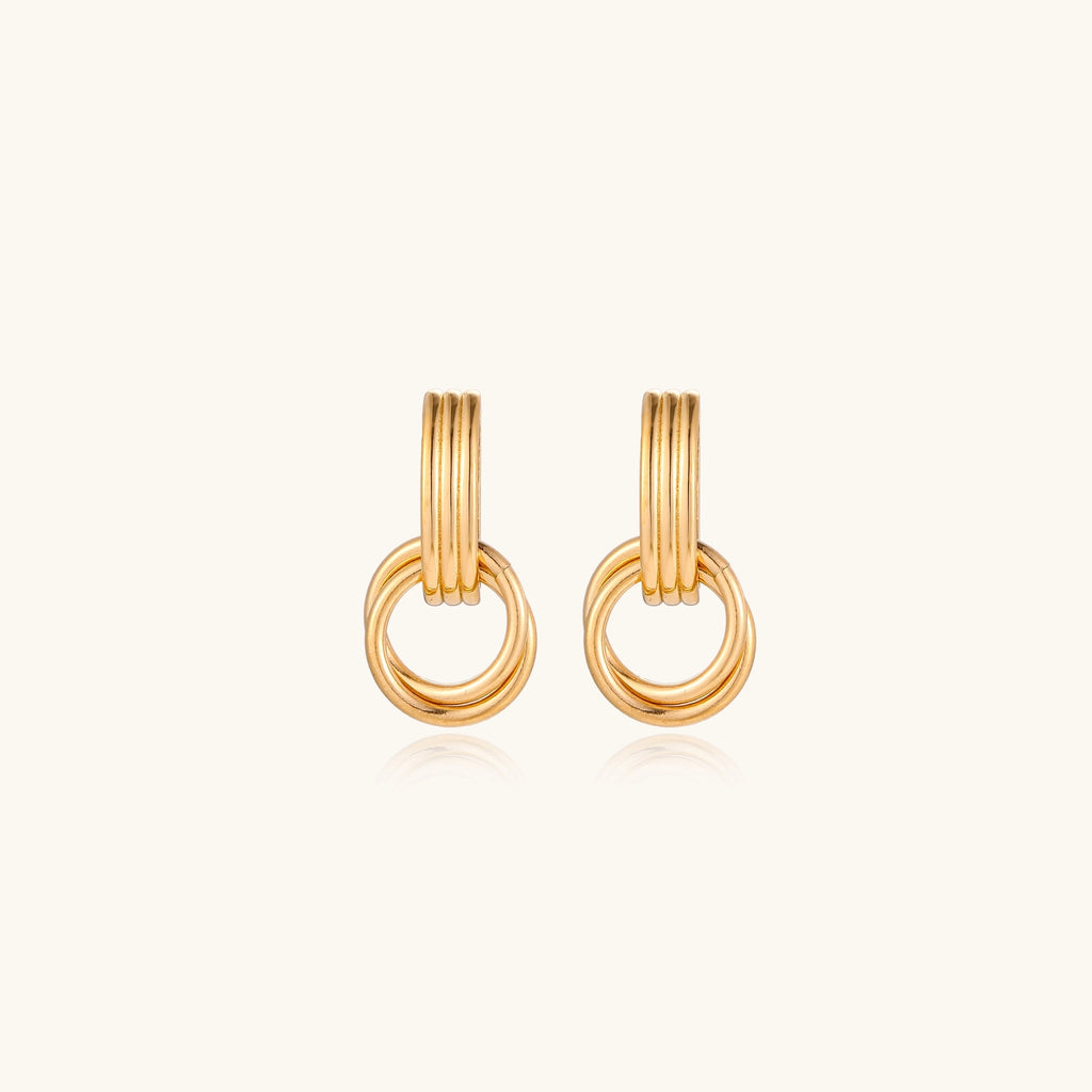 Geometric gold earrings with ribbed linear top section and circular drop elements on white background.