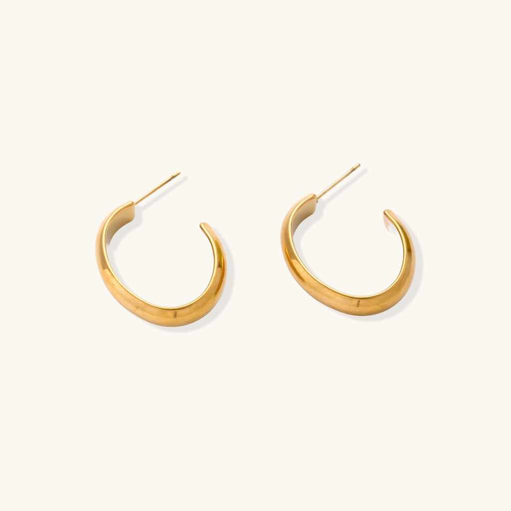 Four pairs of gold-plated stainless steel earrings including hoops and studs displayed on cream background