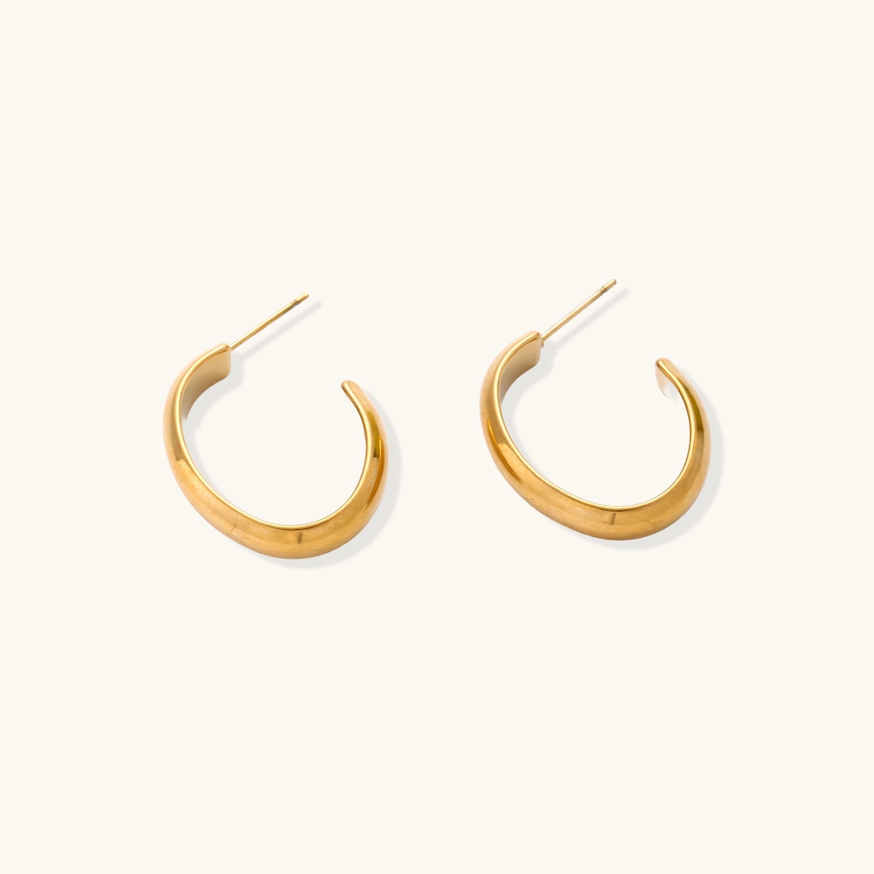 Four pairs of gold-plated stainless steel earrings including hoops and studs displayed on cream background