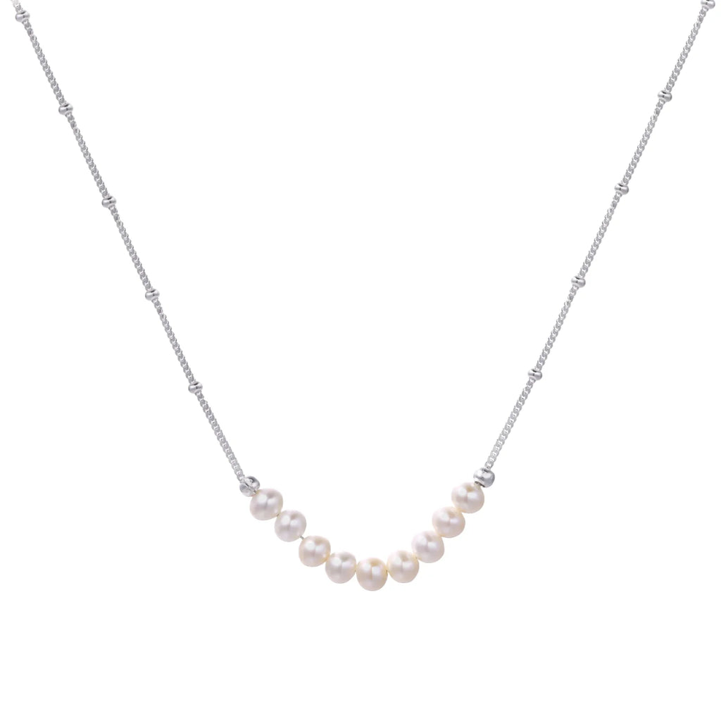 Delicate sterling silver chain necklace with small freshwater pearls arranged in a curved smile arc on cream background.