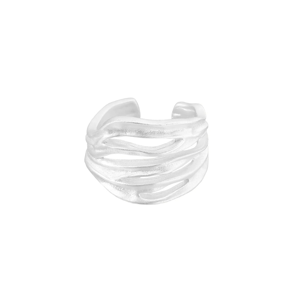Wide sterling silver cuff ring with flowing wave patterns creating dimensional texture against cream background
