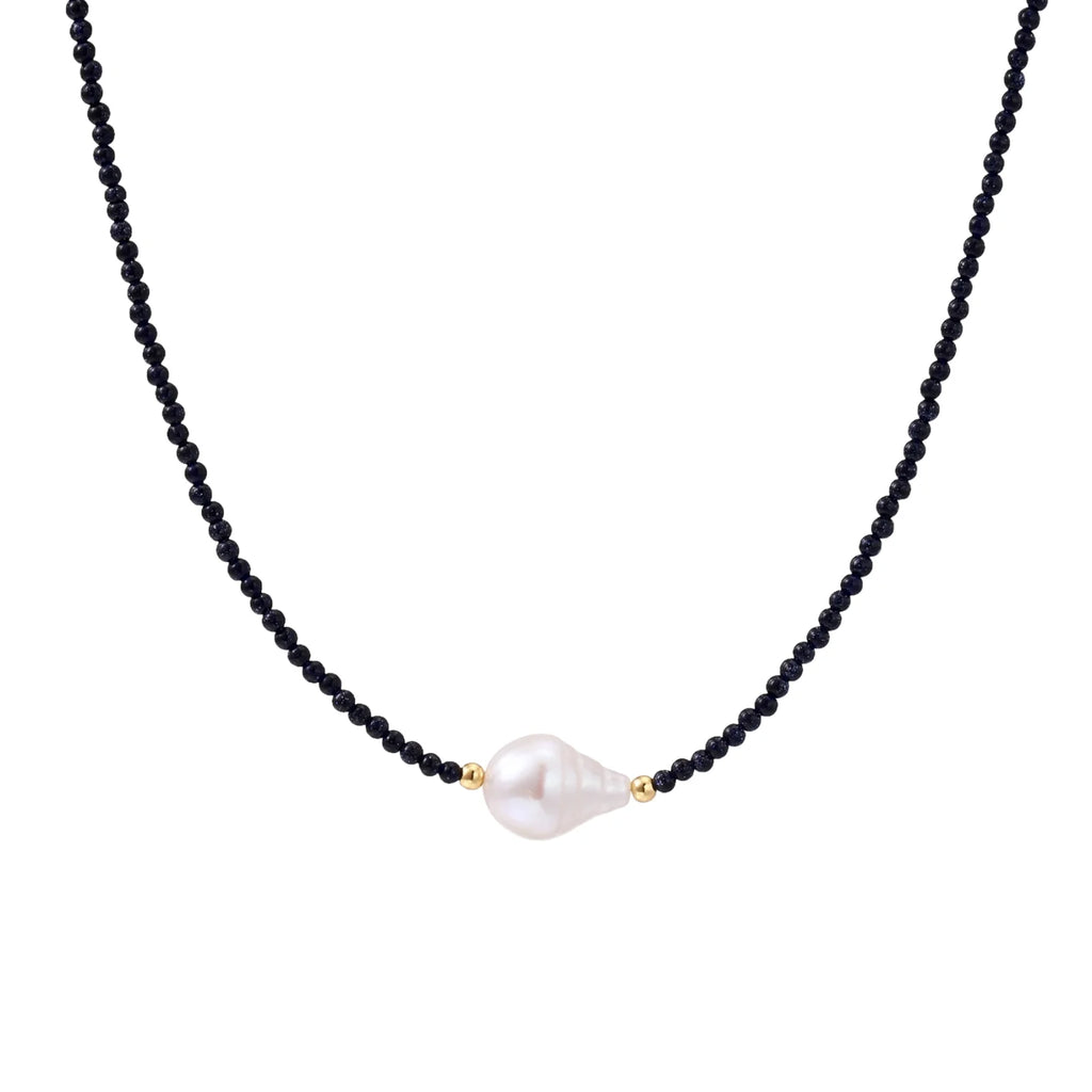 Delicate necklace with black blue sandstone beads and baroque pearl center on white background with gold accents.