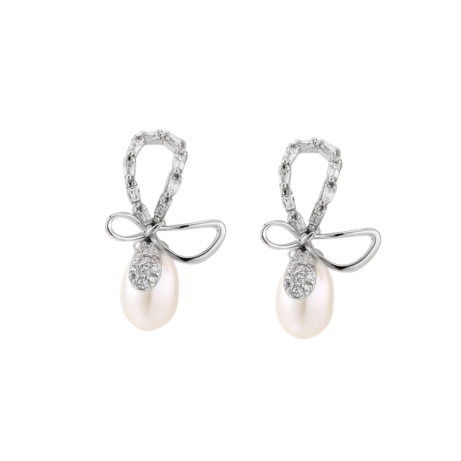 Silver bow-shaped stud earrings with baguette crystals and dangling white freshwater pearls on cream background
