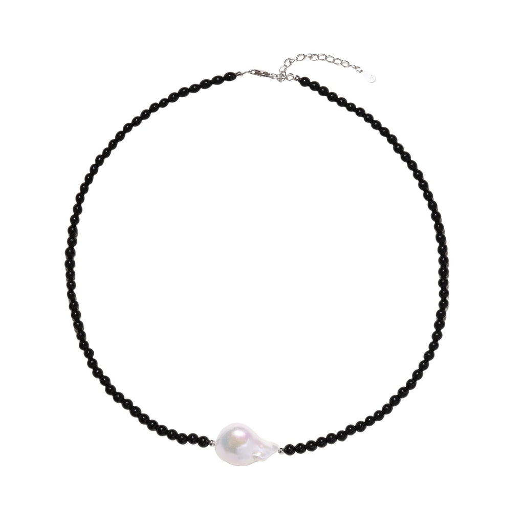 Beaded black agate necklace with iridescent baroque freshwater pearl centerpiece on cream background.